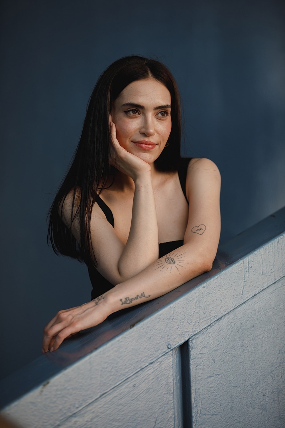 Woman with tattoos leaning on railing, thoughtful expression.