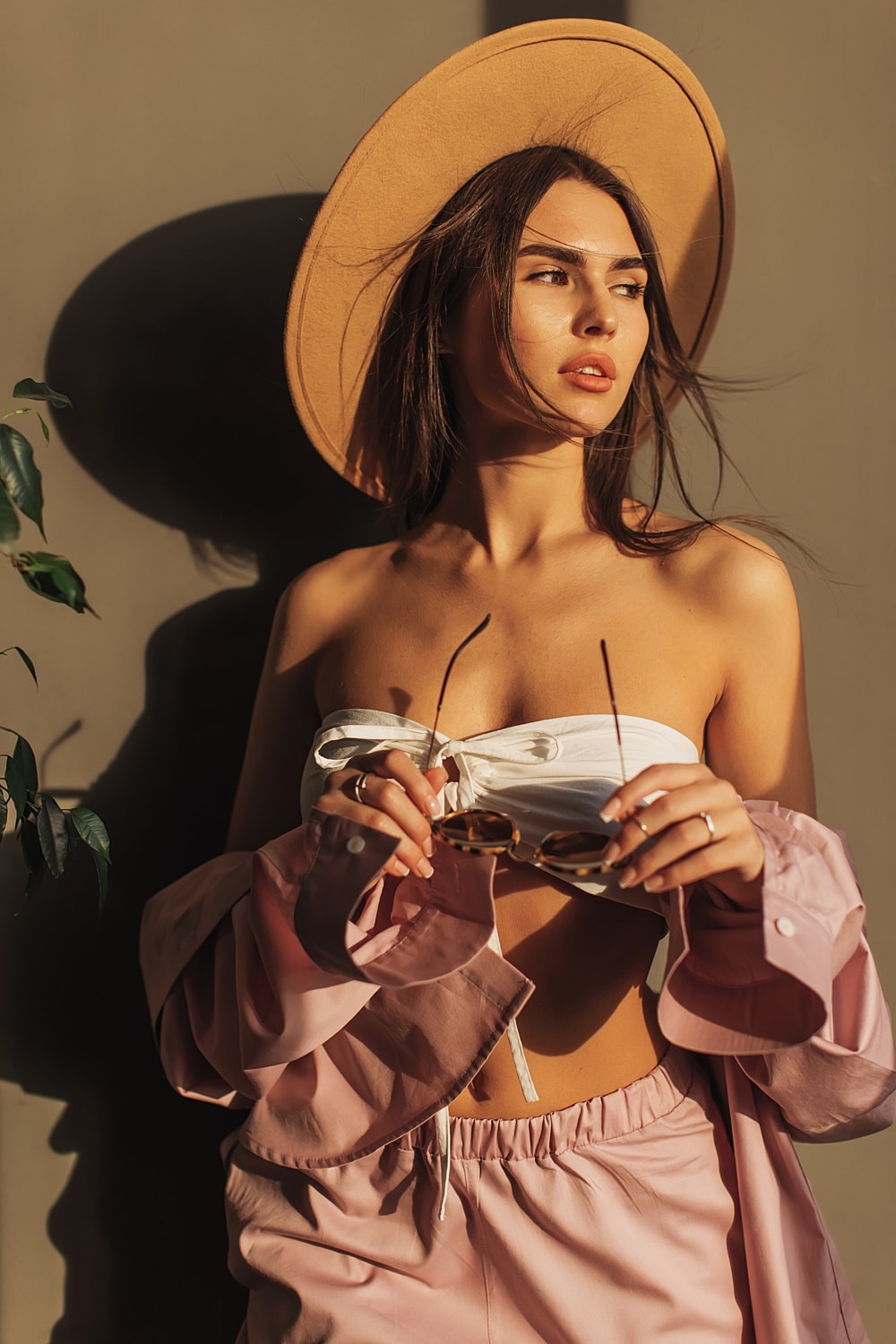 Woman in hat posing with sunglasses and plants.