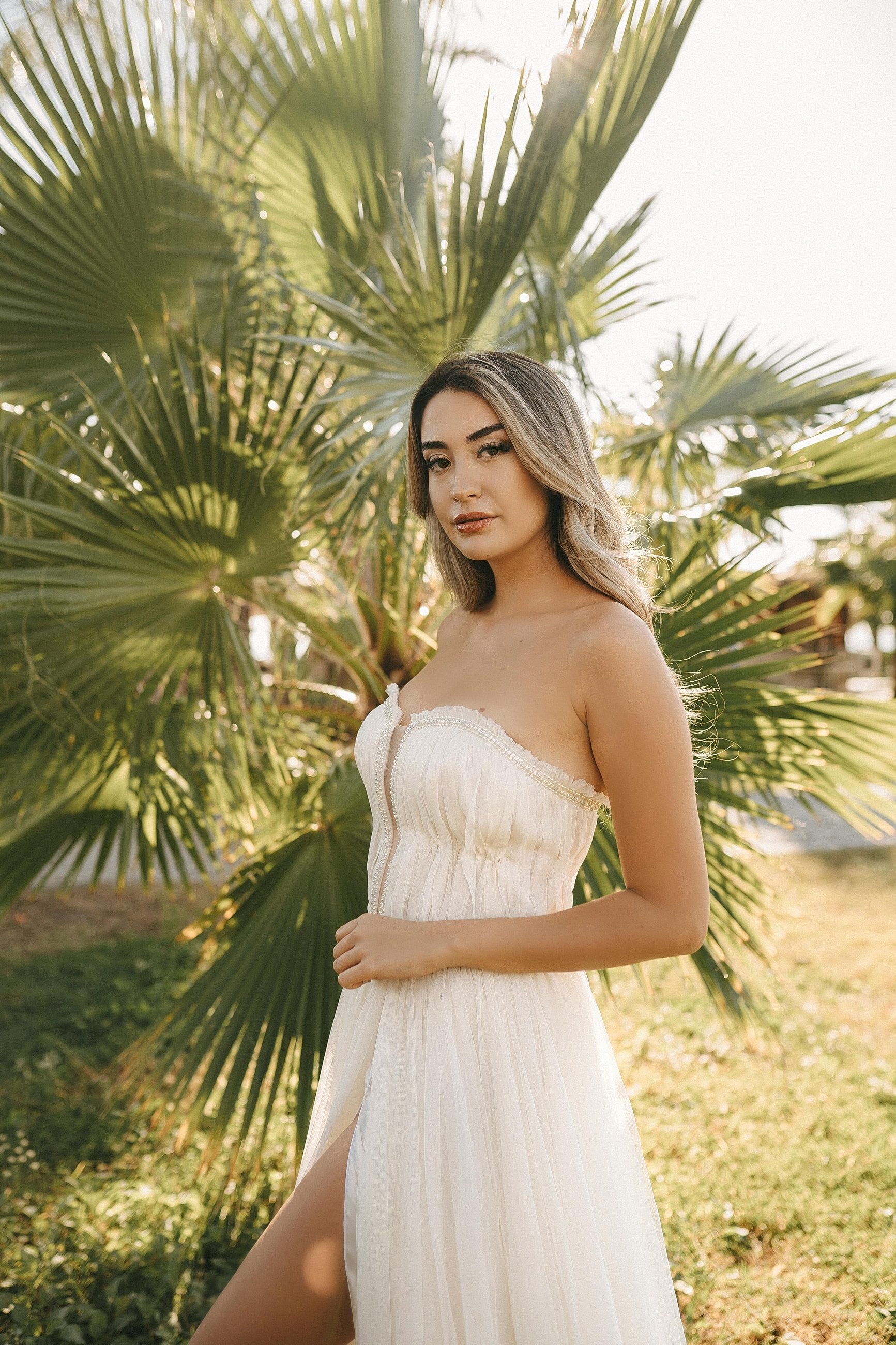 Woman in white dress near palm trees.