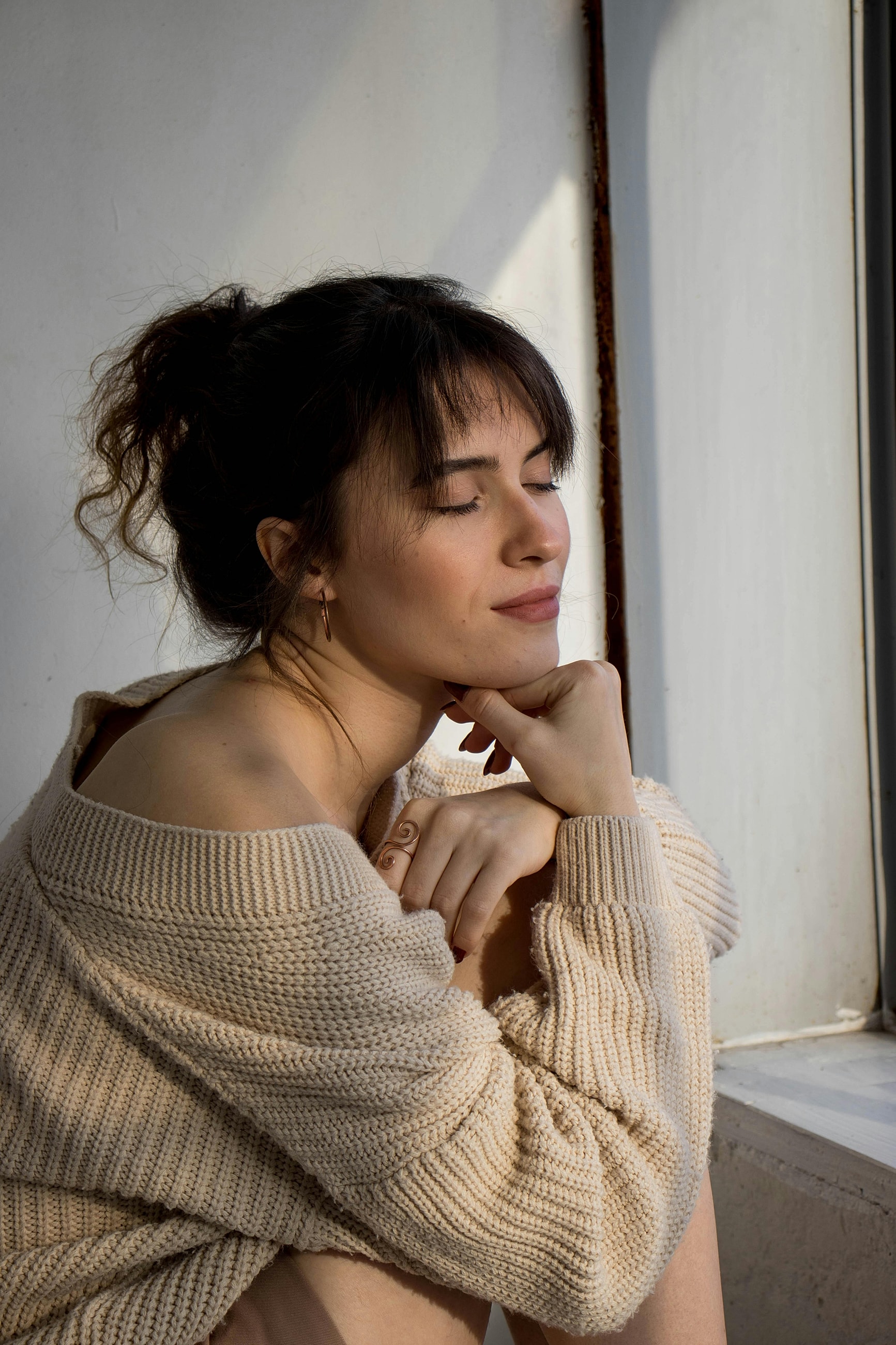 Woman in sweater, eyes closed, thoughtful expression.