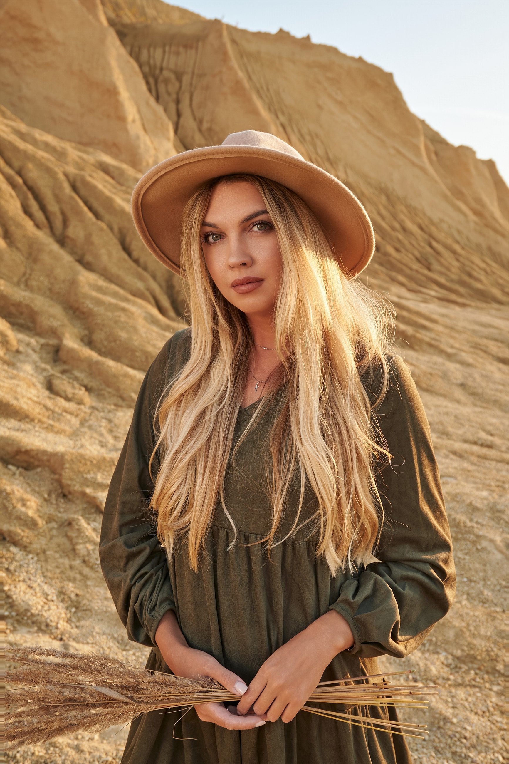Woman in green dress holding dried grass.